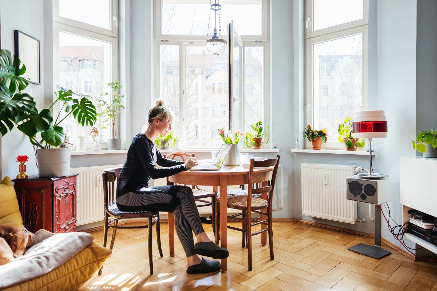 A single mom sitting in a well light and modern living room at a wooden table using her laptop.