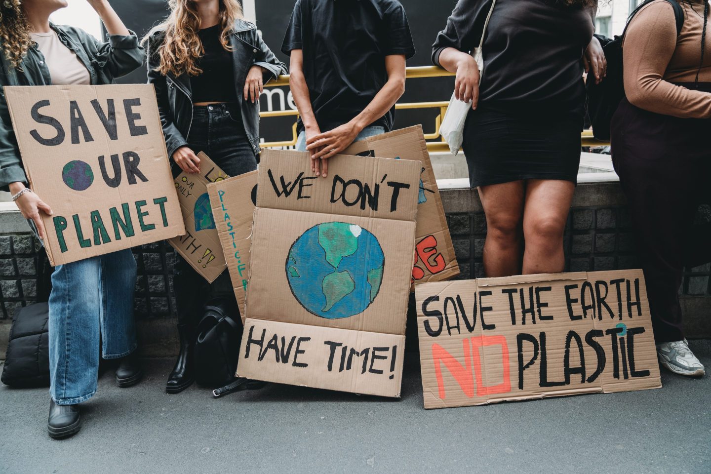 People at a climate protest holding cardboard signs that read, "Save our planet," and "We don't have time," and "Save the Earth, no plastic."