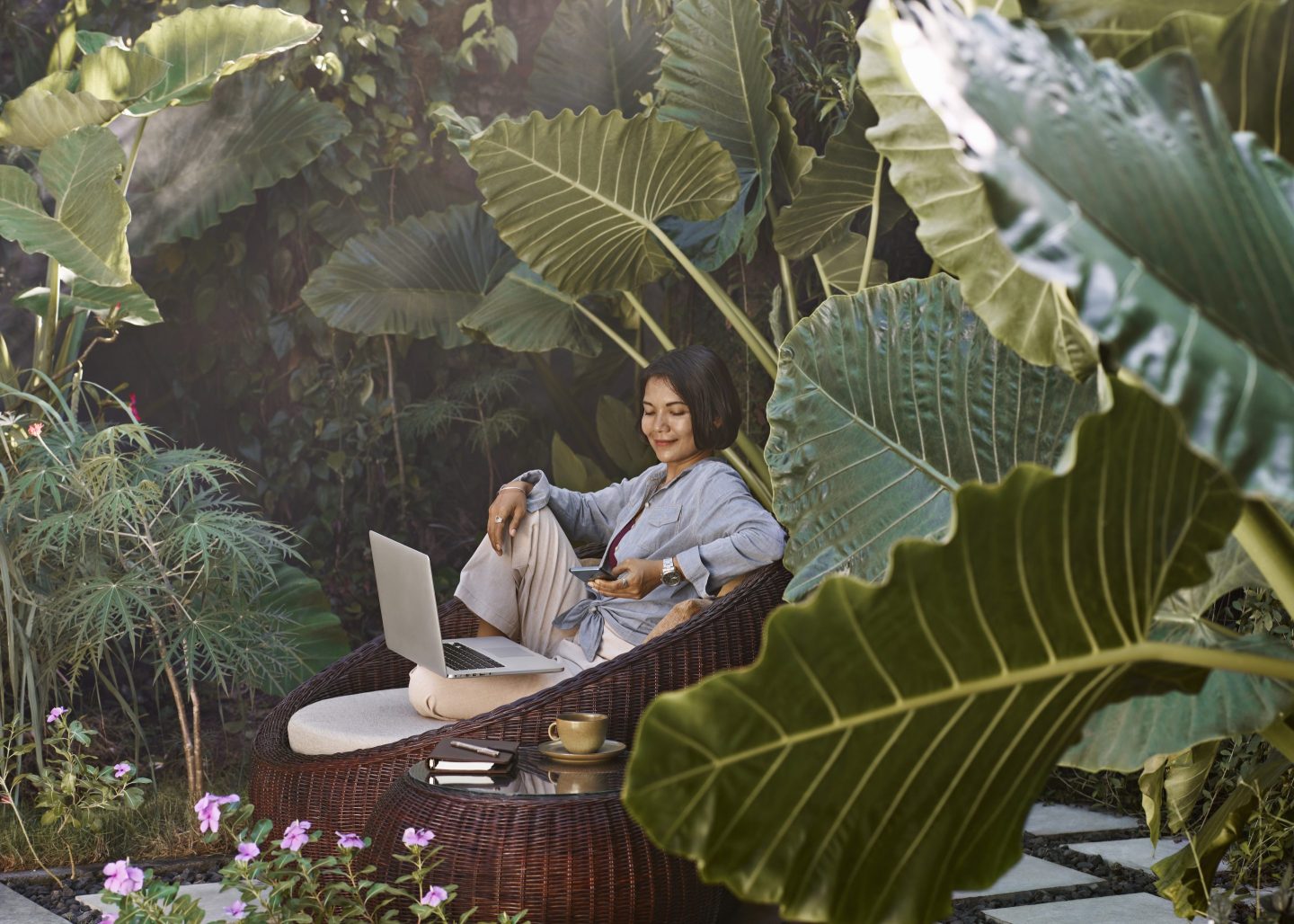 A woman in Bali working from home sitting in garden furniture surrounded by tropical plants