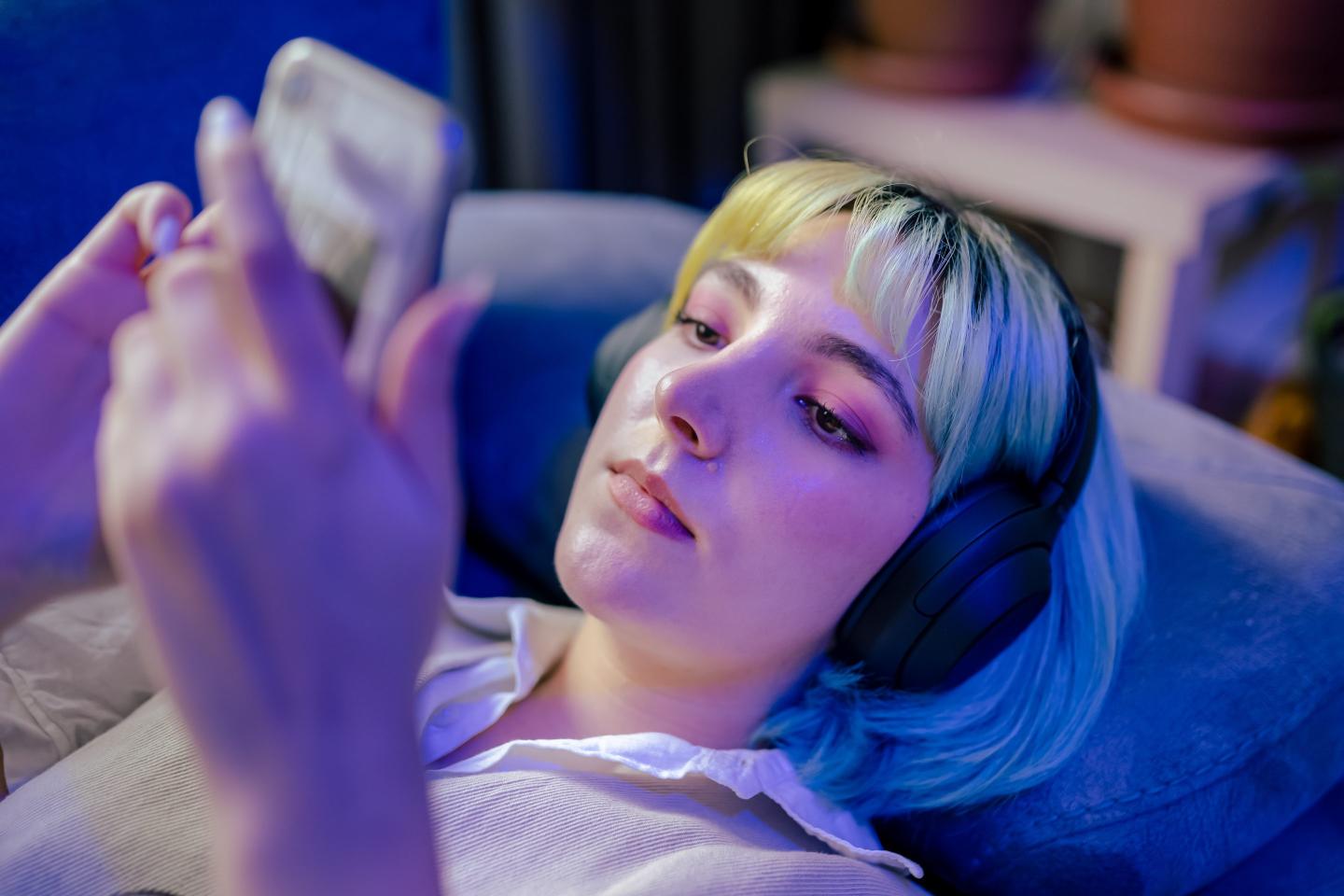 Beautiful teenage girl standing next to neon light and listening music