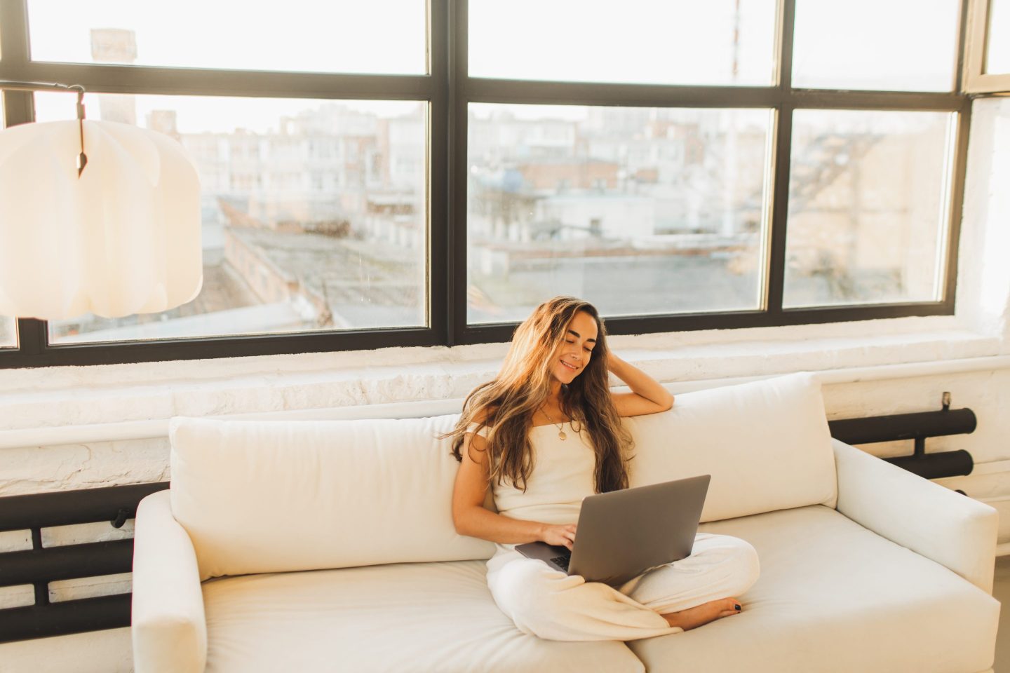 Young woman sitting on sofa with legs crossed and working on laptop computer