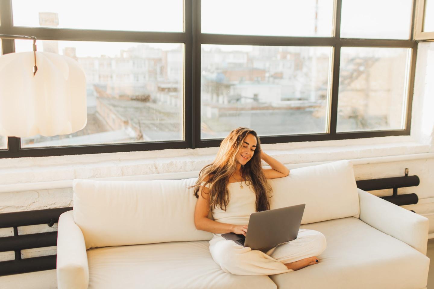 Young woman sitting on sofa with legs crossed and working on laptop computer