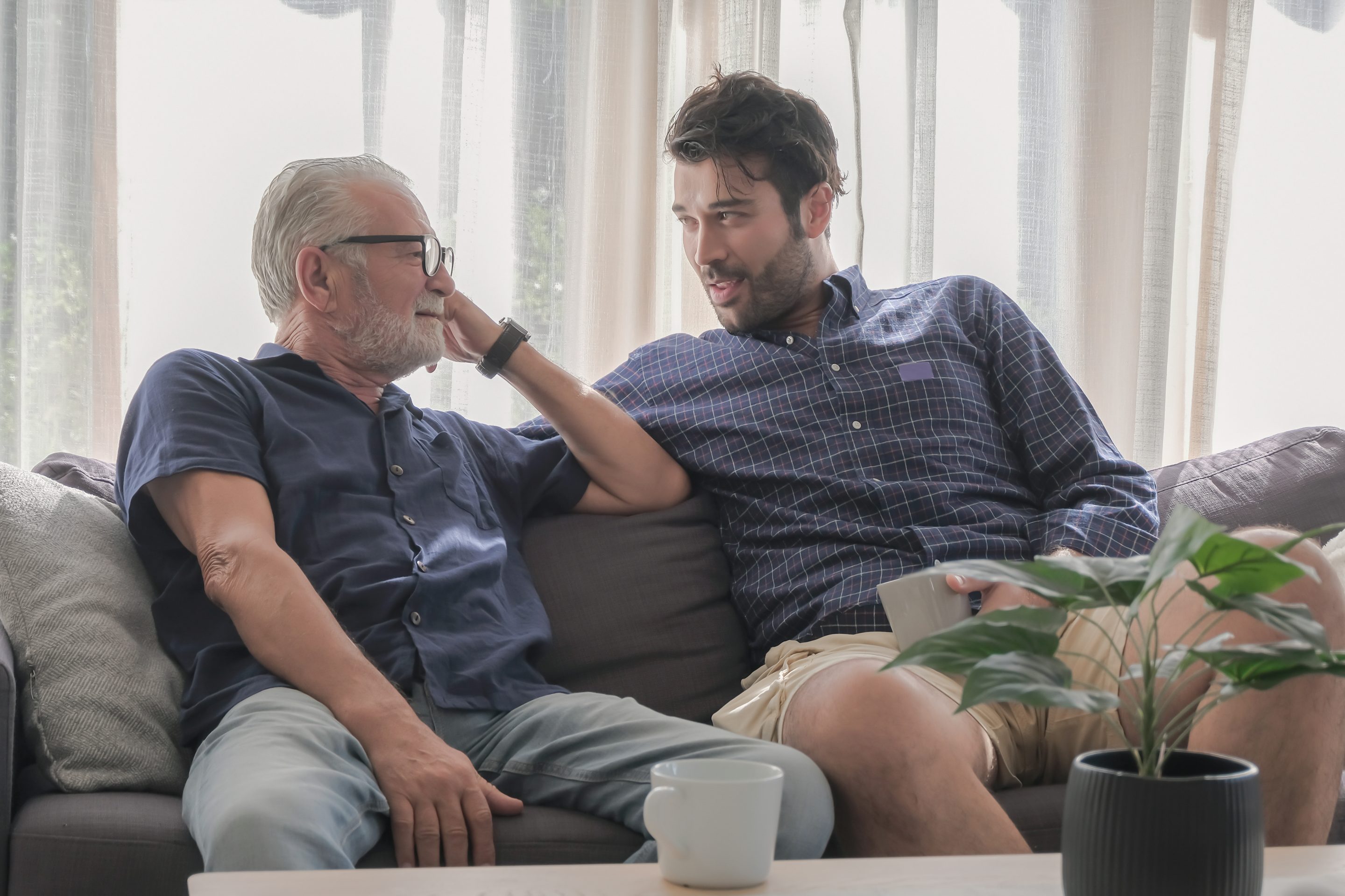 An older man and a younger man are sitting on sofa together