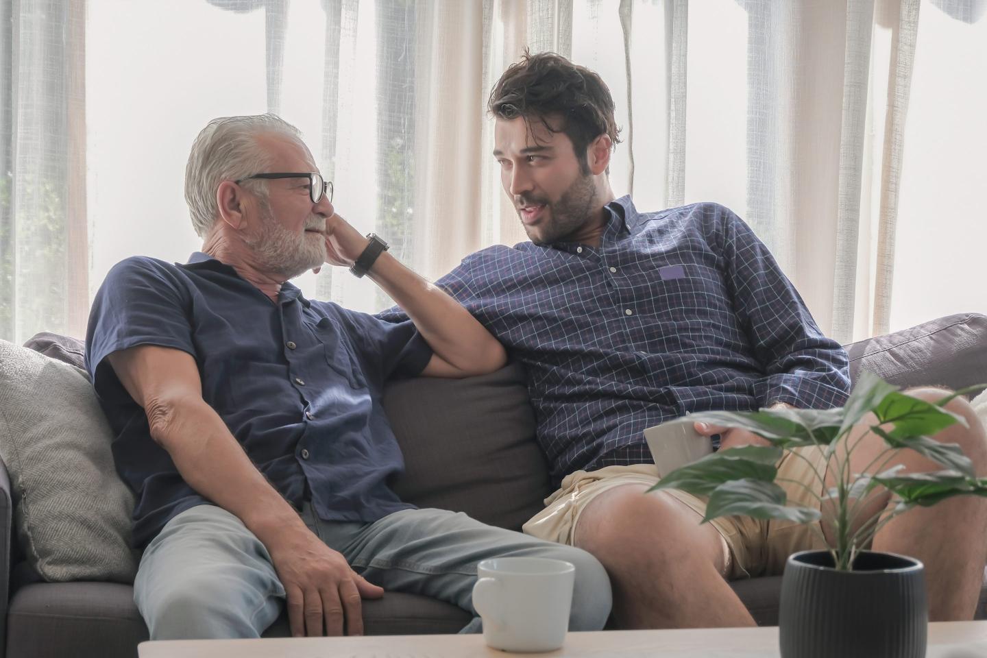 An older man and a younger man are sitting on sofa together