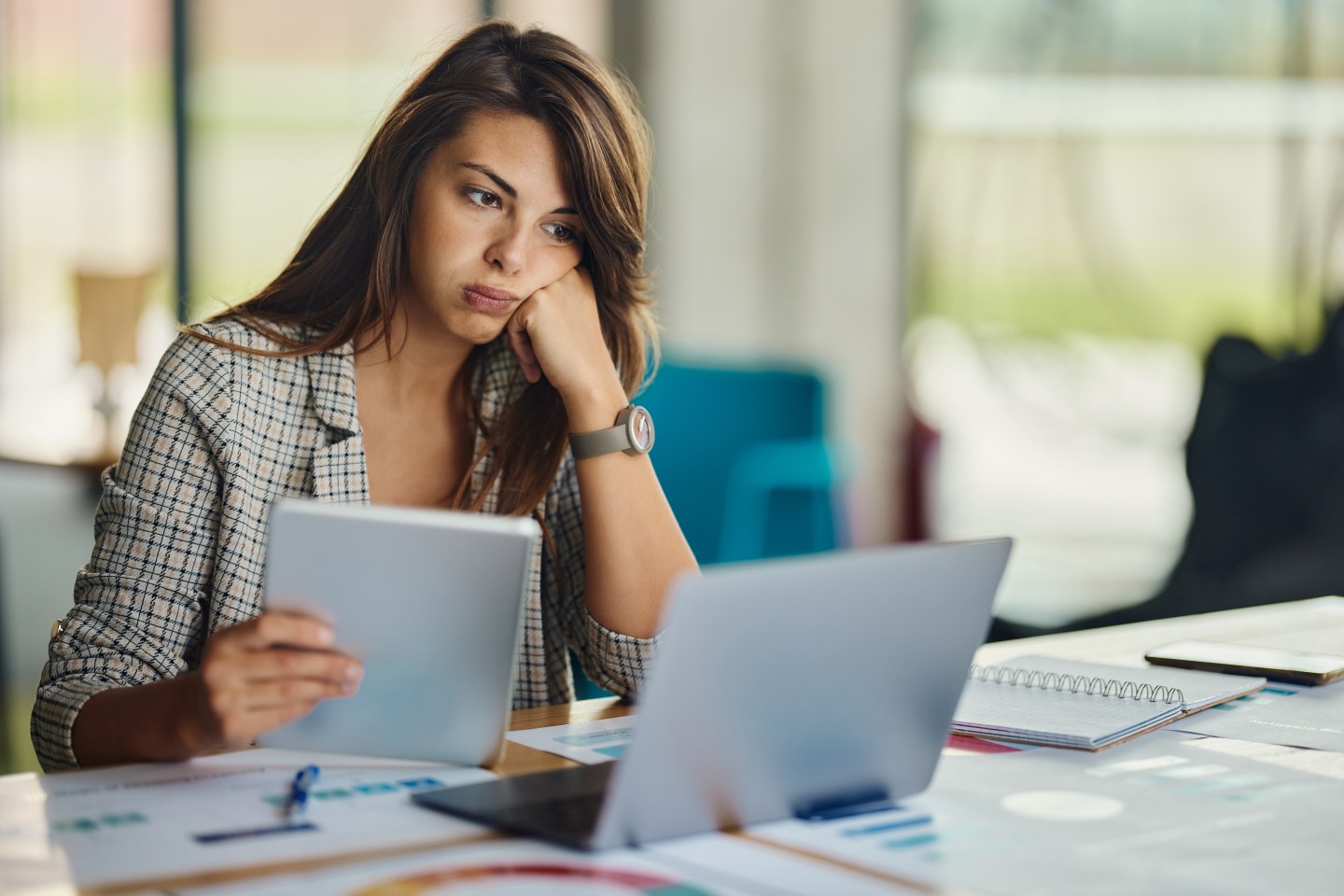 Young businesswoman brainstorming while working on digital tablet and laptop in the office.