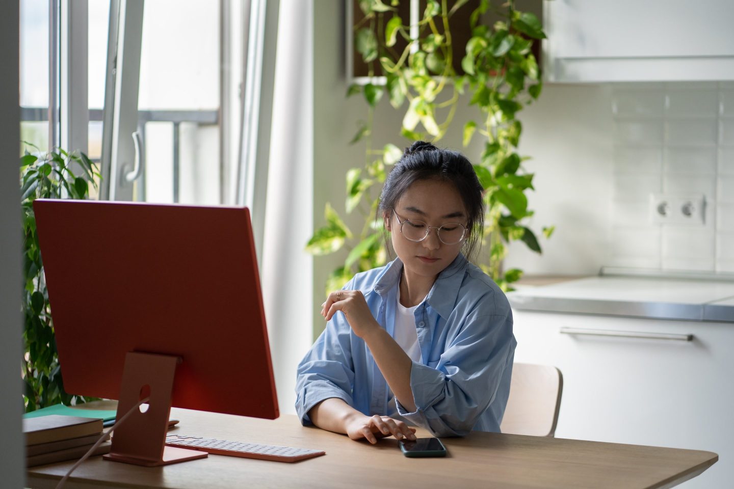 Young Asian woman remote worker wearing glasses touching smartphone screen checking phone while working remotely, push notifications and freelance productivity. Online learning distractions at home