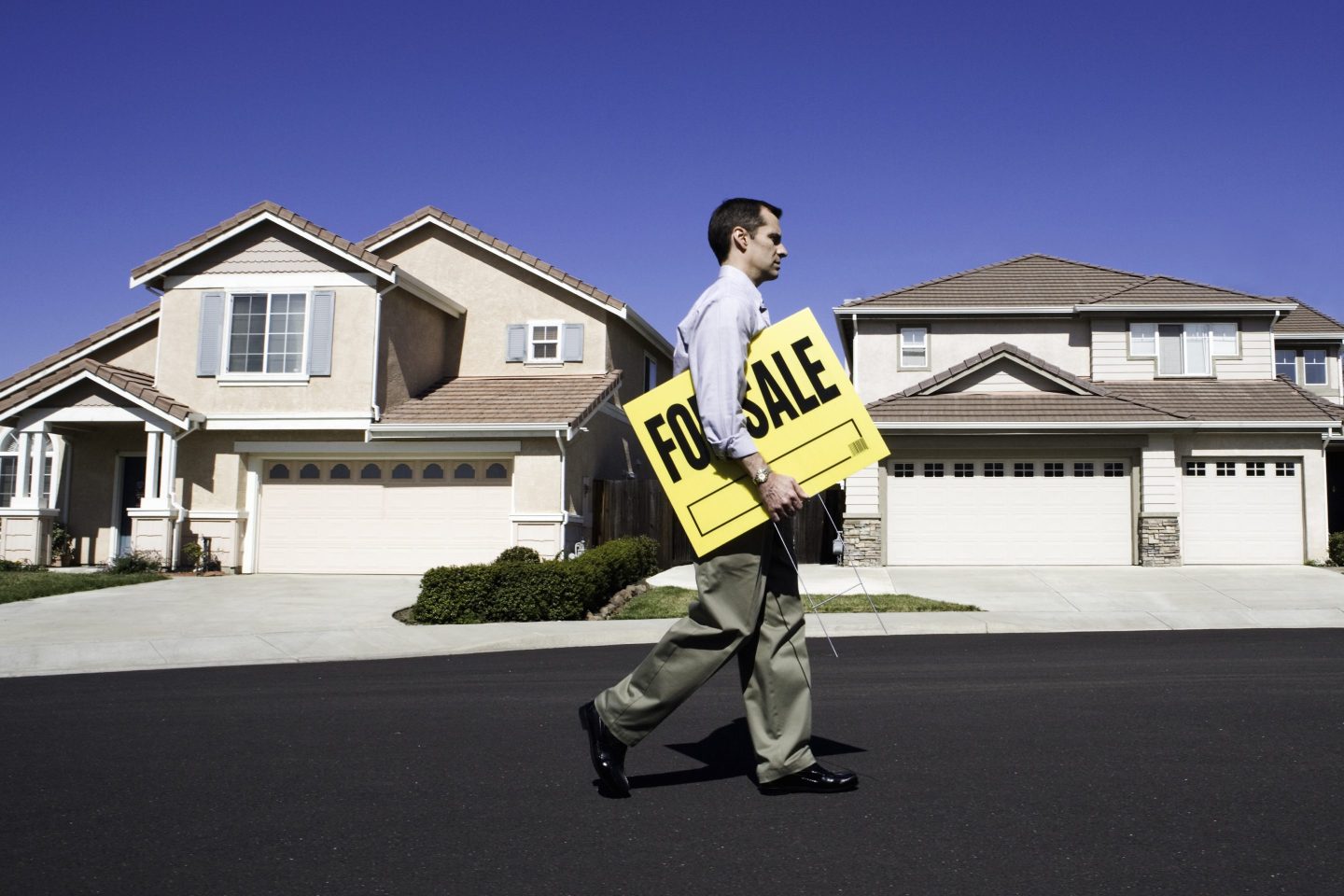 Man carrying a for-sale sign in a development of single-family homes