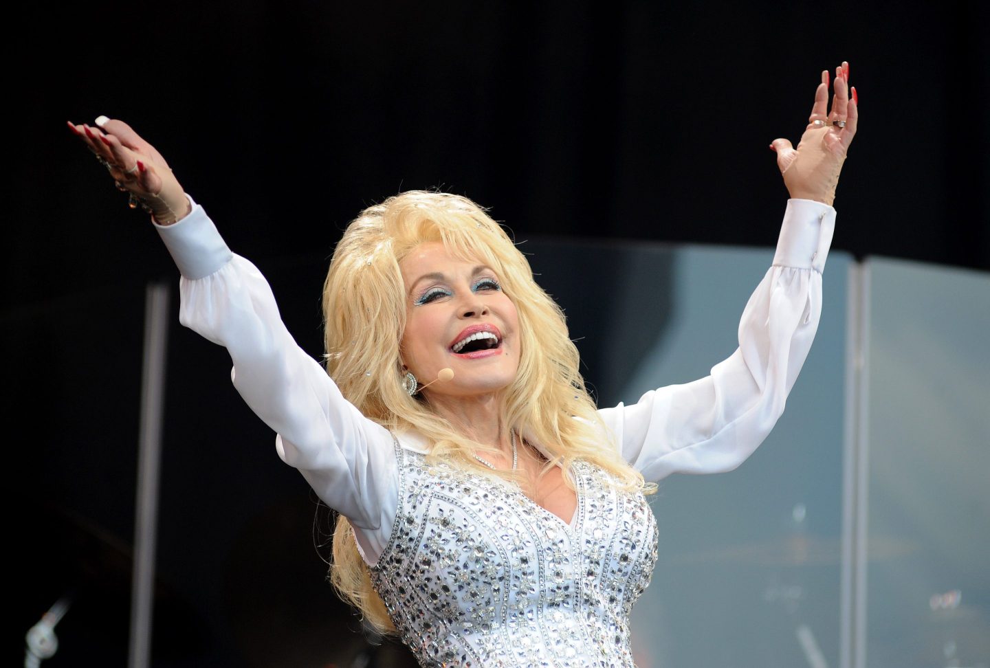 Dolly Parton performing on stage in a white, rhinestone outfit