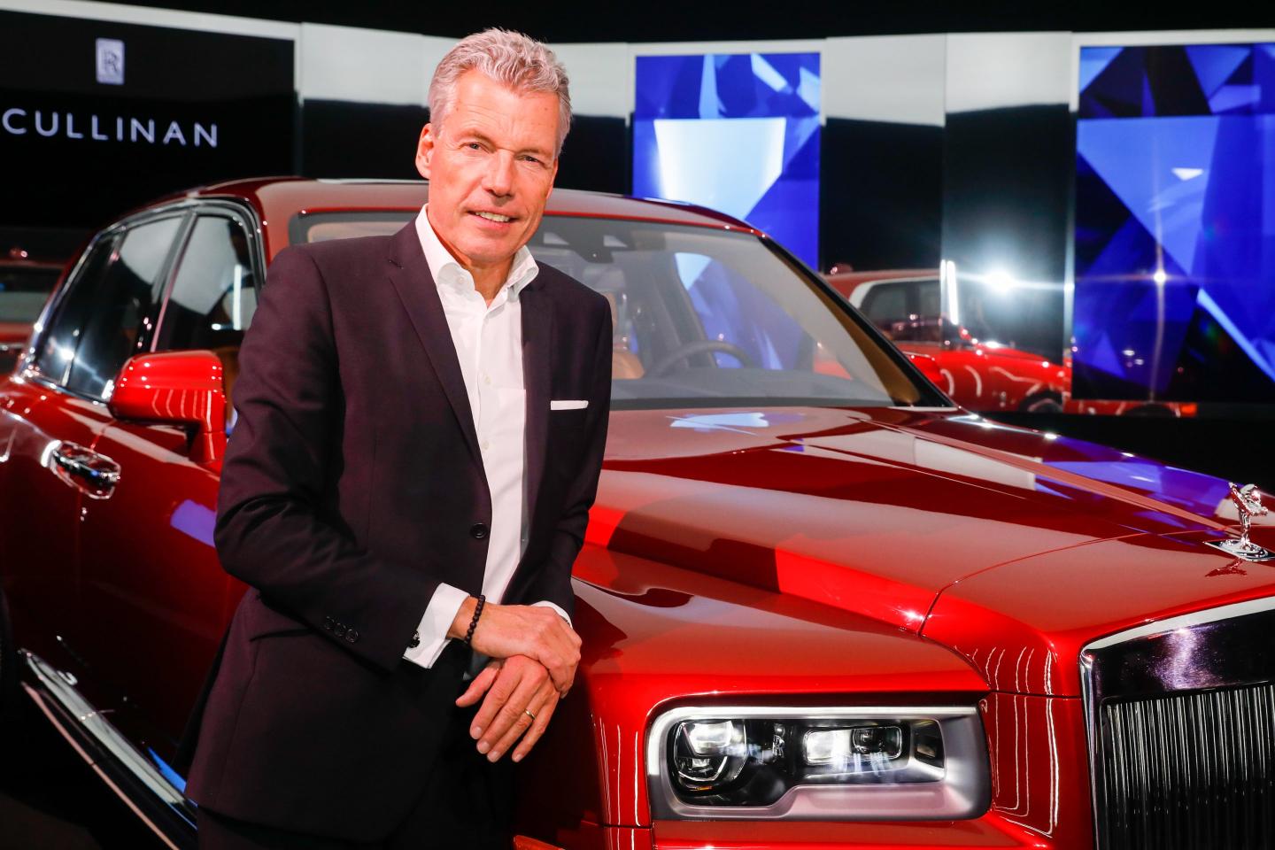 Torsten Muller-Otvos pictured next to a red rolls-royce car