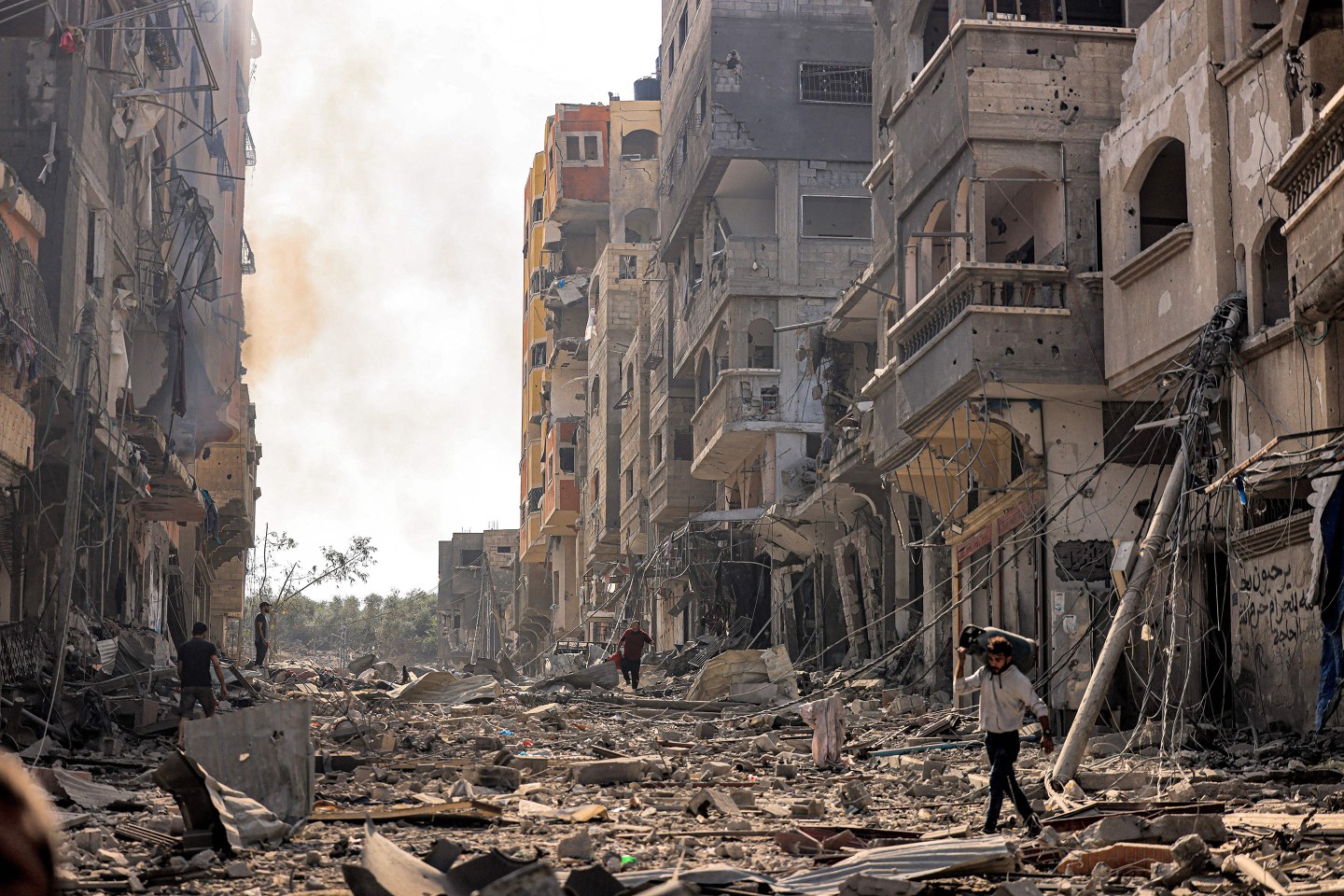 A man carries a propane gas cylinder on his back while walking through debris and destruction littering a street in the Jabalia camp for Palestinian refugees in Gaza City on Oct. 11.