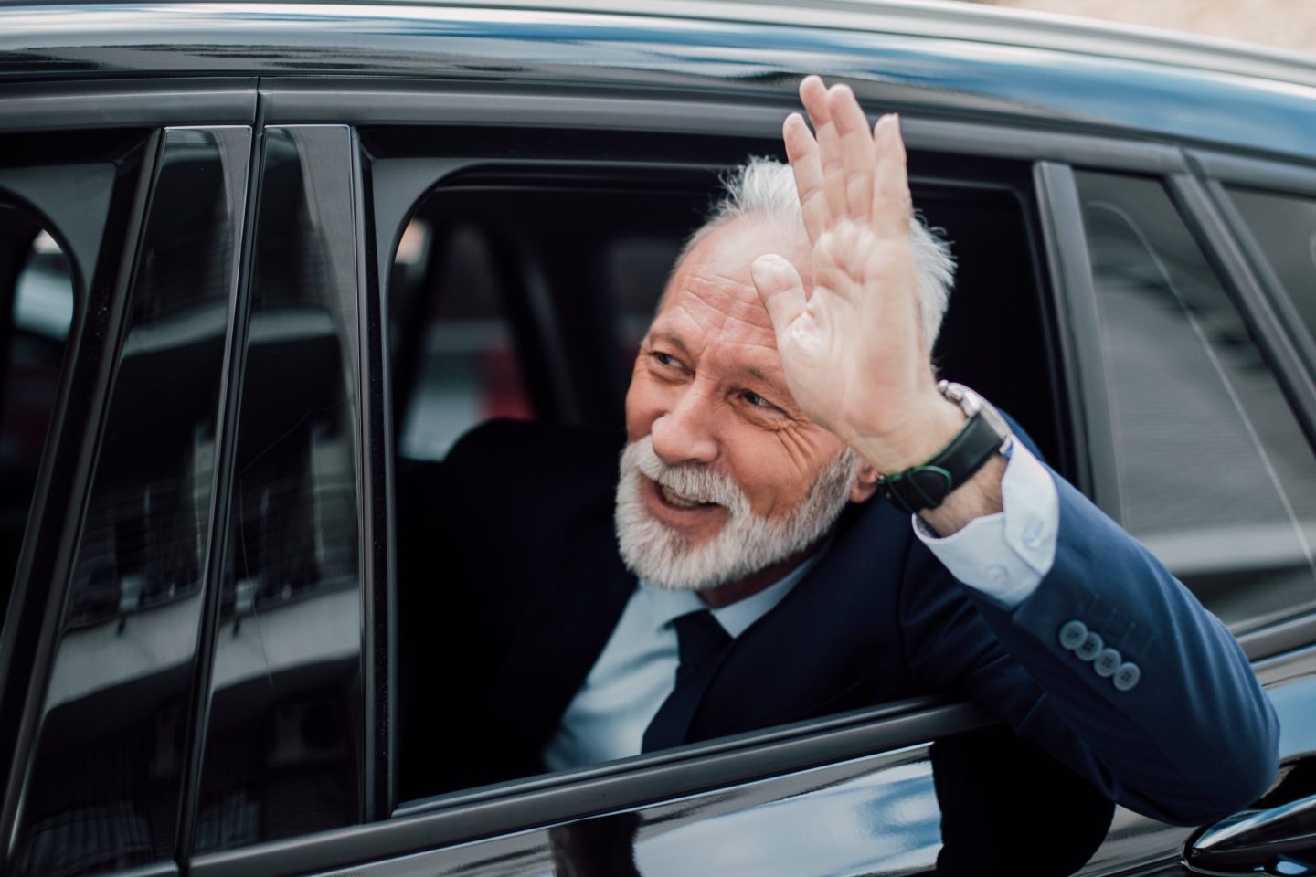A businessman waves from a car