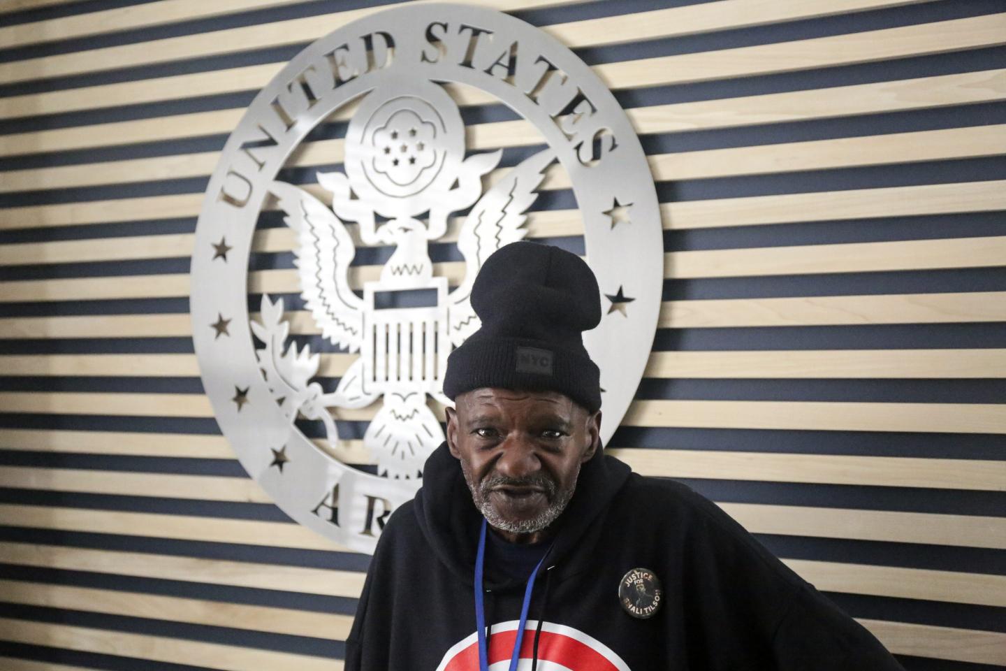 A Vietnam War-era veteran stands in front of a United States Army emblem displayed on the wall behind him