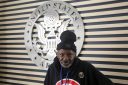 A Vietnam War-era veteran stands in front of a United States Army emblem displayed on the wall behind him