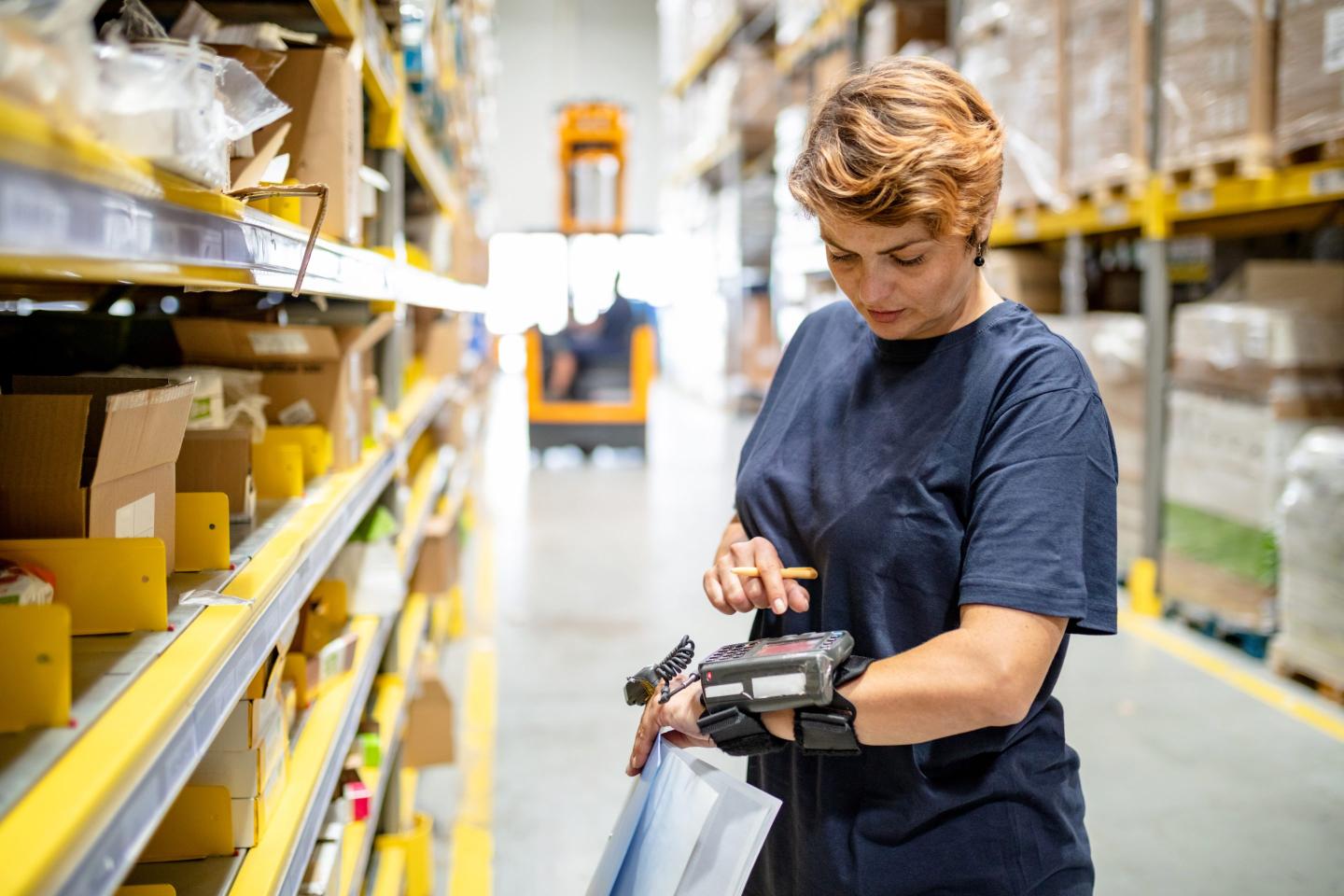 Woman in warehouse pushing buttons on wearable barcode reader.