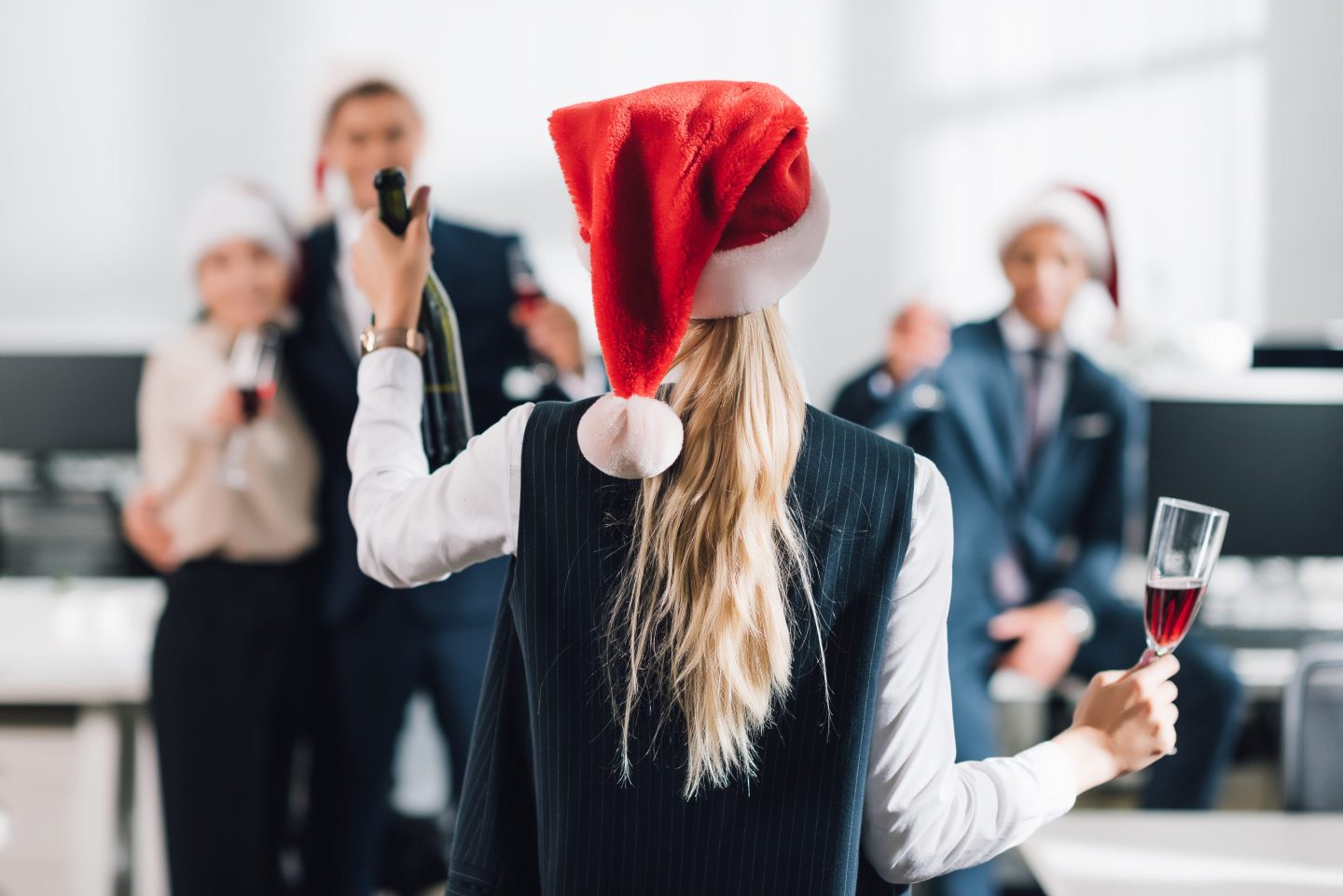 A person wearing a Father Christmas hat raises a glass to colleagues
