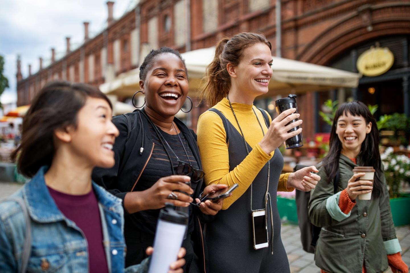 Happy female friends with drinks walking in city