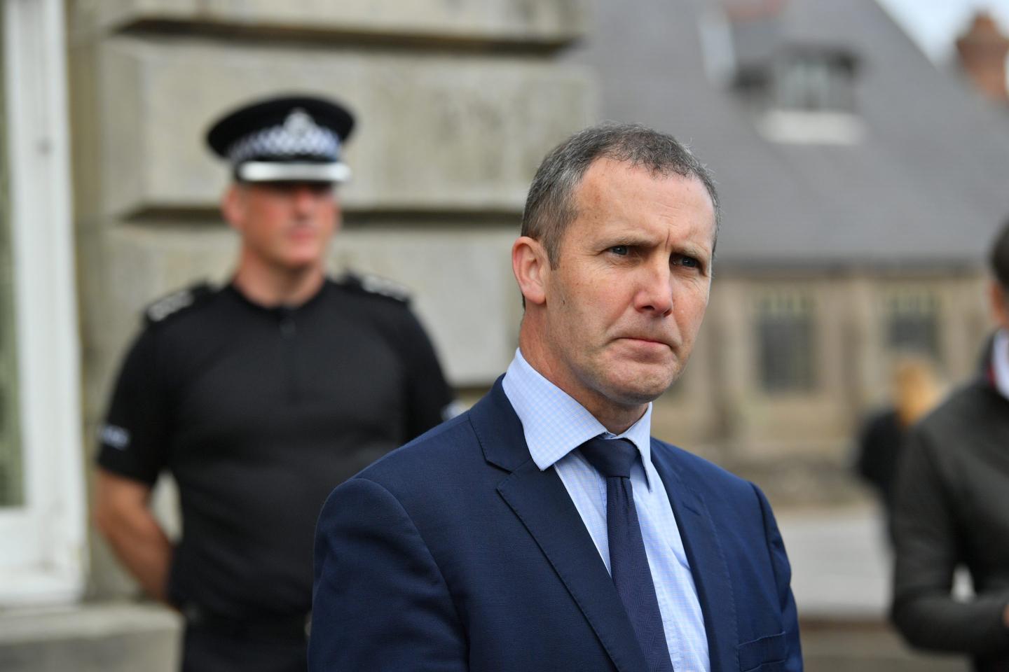 michael matheson in a suit with police officers in the background