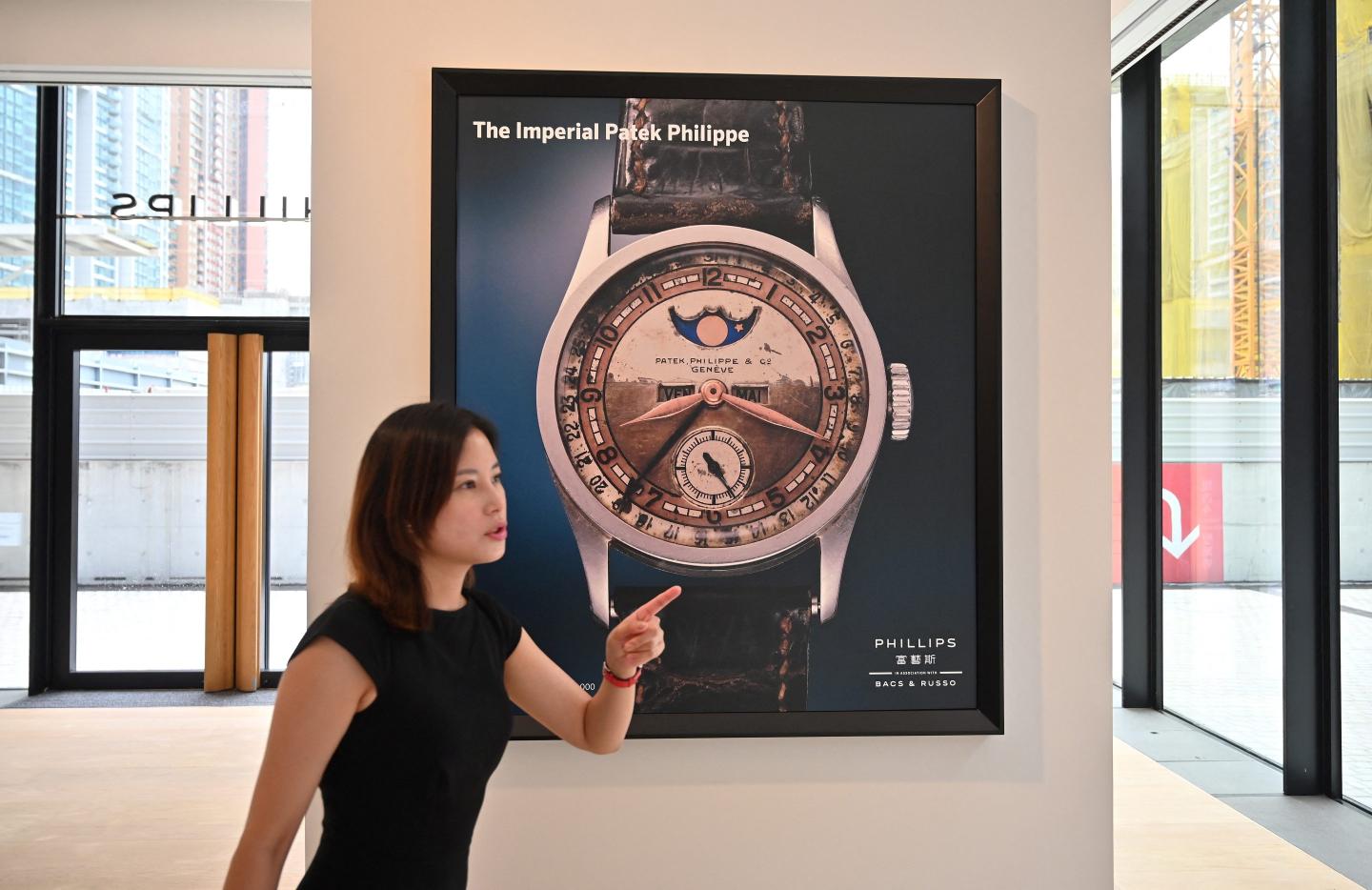 a lady pointing her finger to the right in front of a poster of a watch