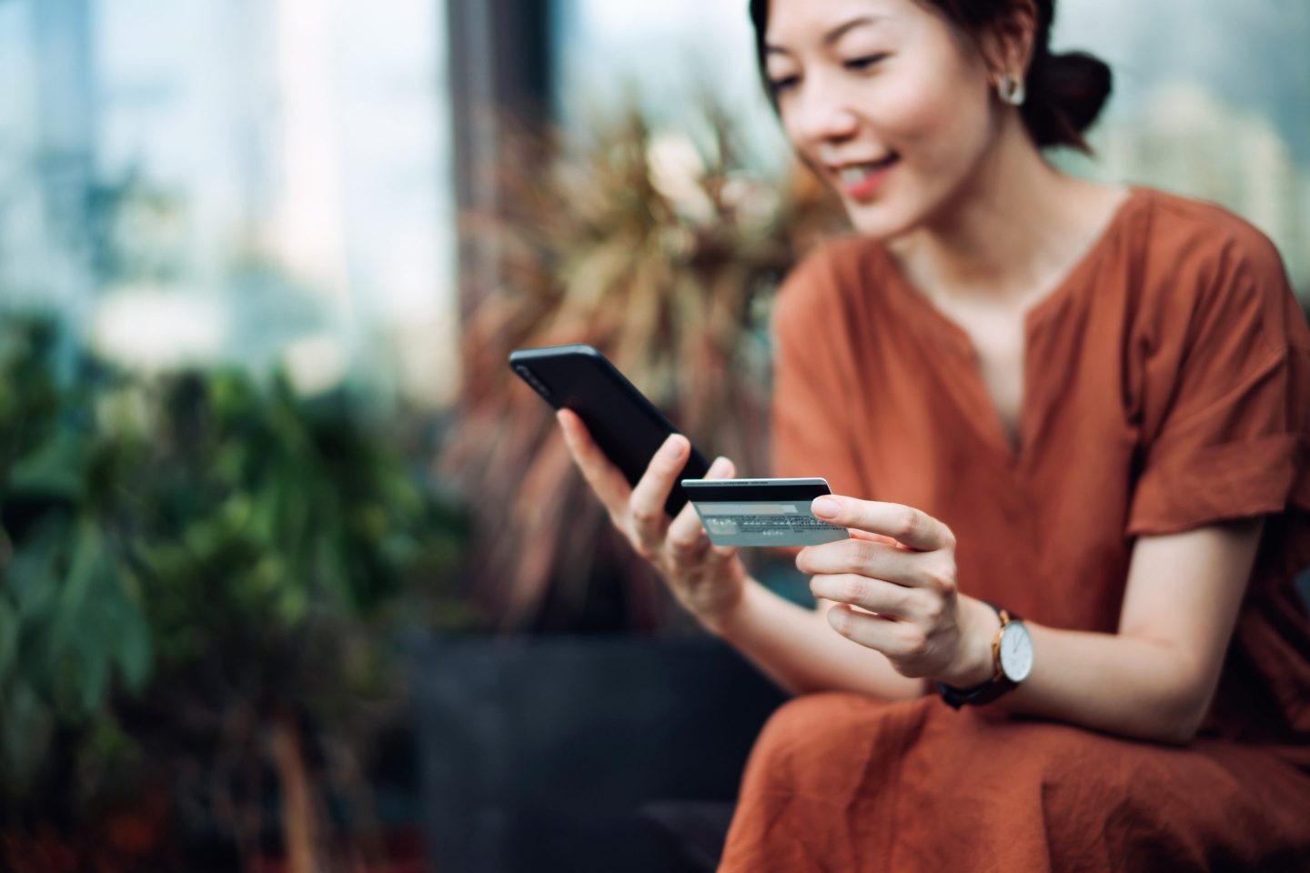Woman using phone and credit card outside on bench