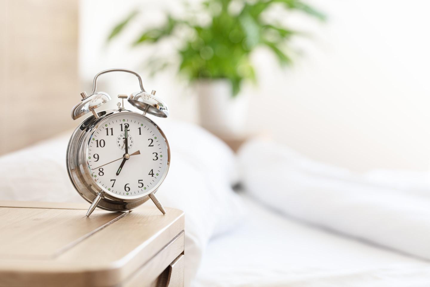 Alarm clock morning wake-up time on bedside table by bed background