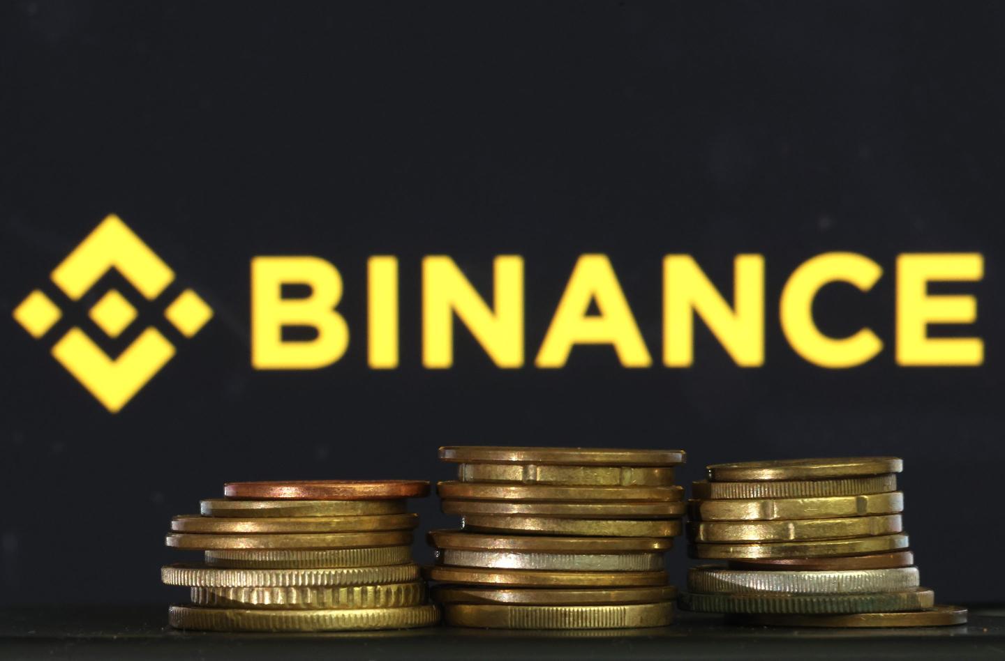 The Binance logo is positioned over three piles of coins
