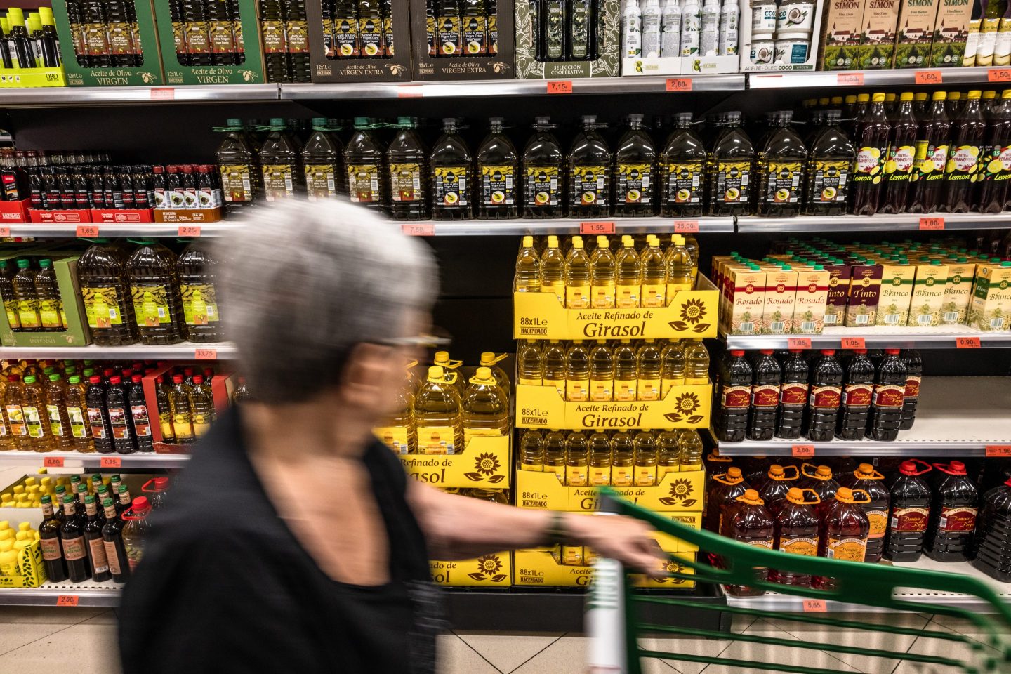 person walking down a supermarket aisle of olive oil shelves