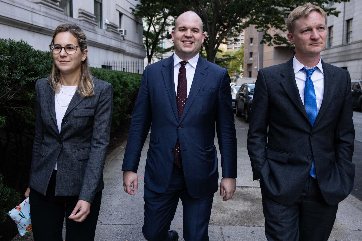 A woman and two men in business suits walking down the sidewalk