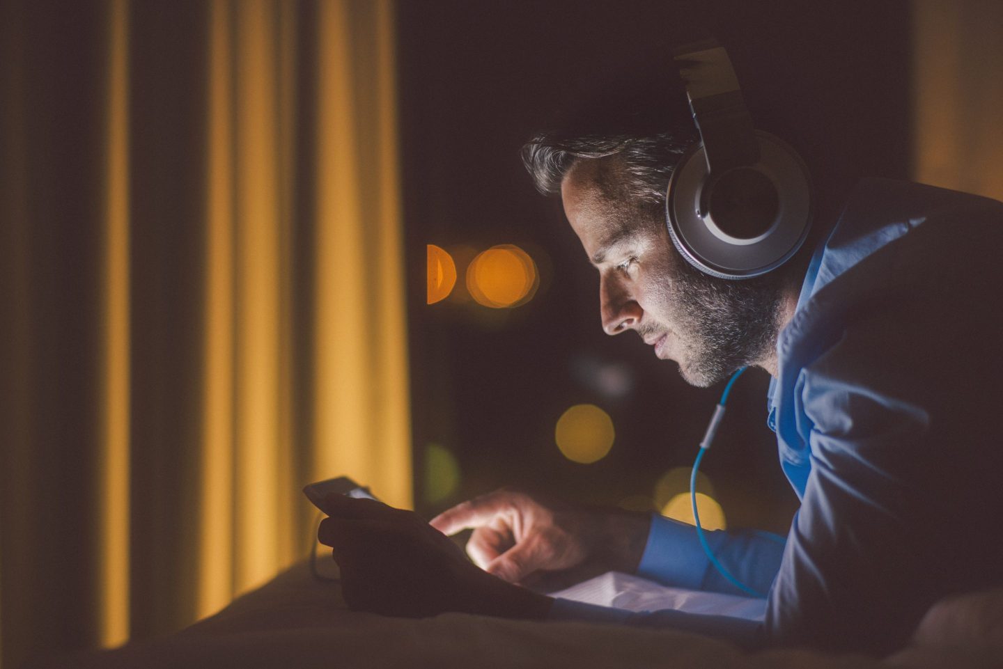 A man listens to content on overhead headphones in a dark room.