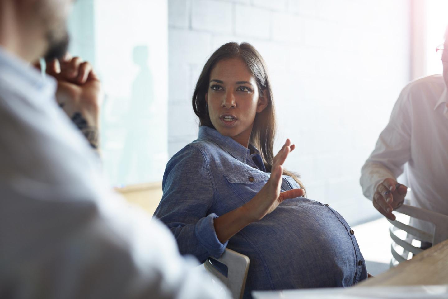 Pregnant woman talking to co-worker, looking annoyed
