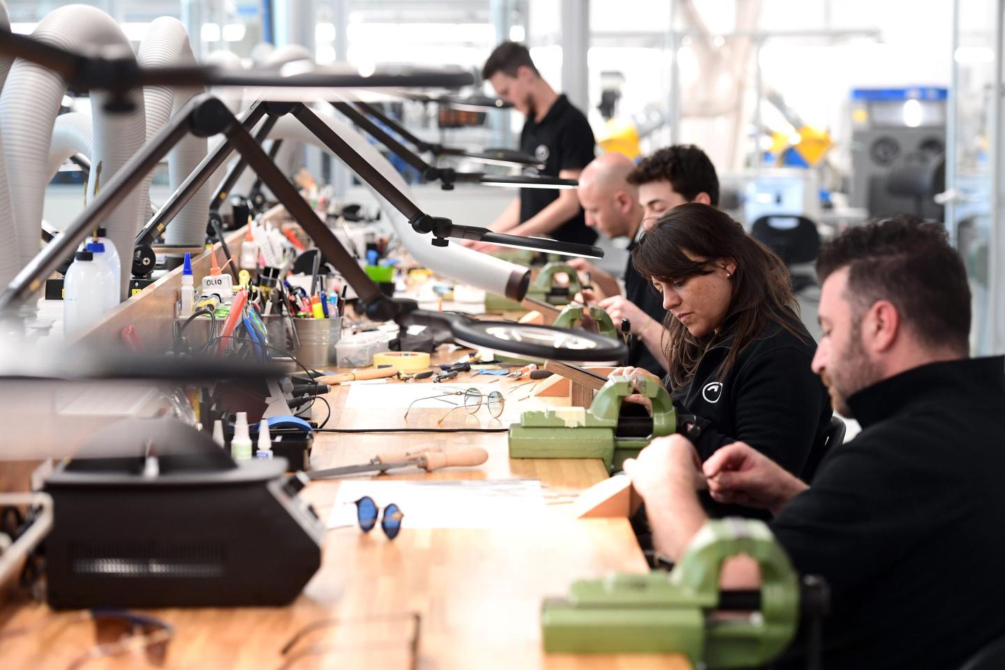 a row of people seen at work with frames for eye glasses in hand