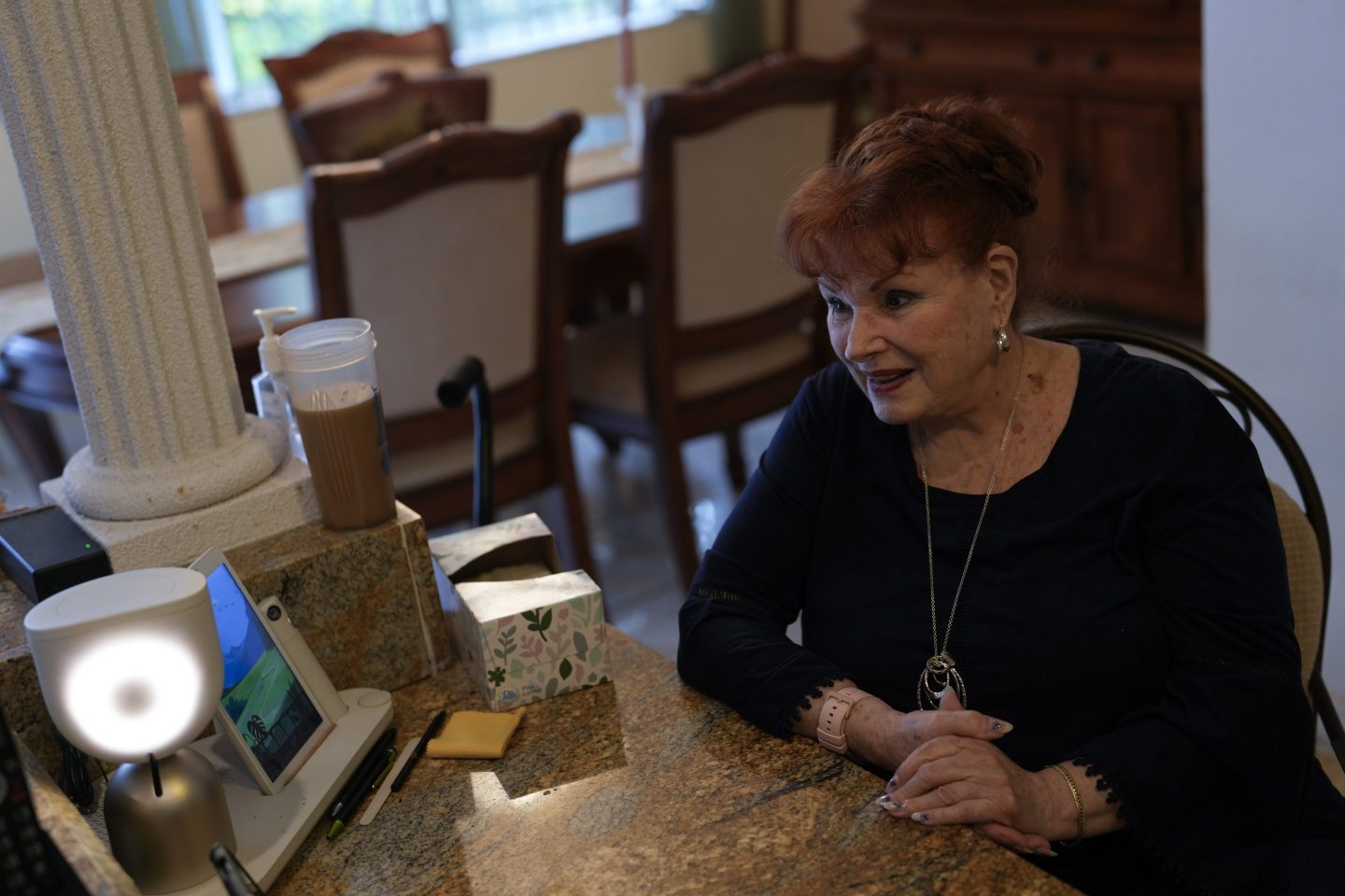 Deanna Dezern, 83, prompts her ElliQ, left, a tabletop device that uses artificial intelligence to conduct human-like conversations, to speak to visiting journalists, inside her home in Tamarac, Fla., on Dec. 7, 2023.