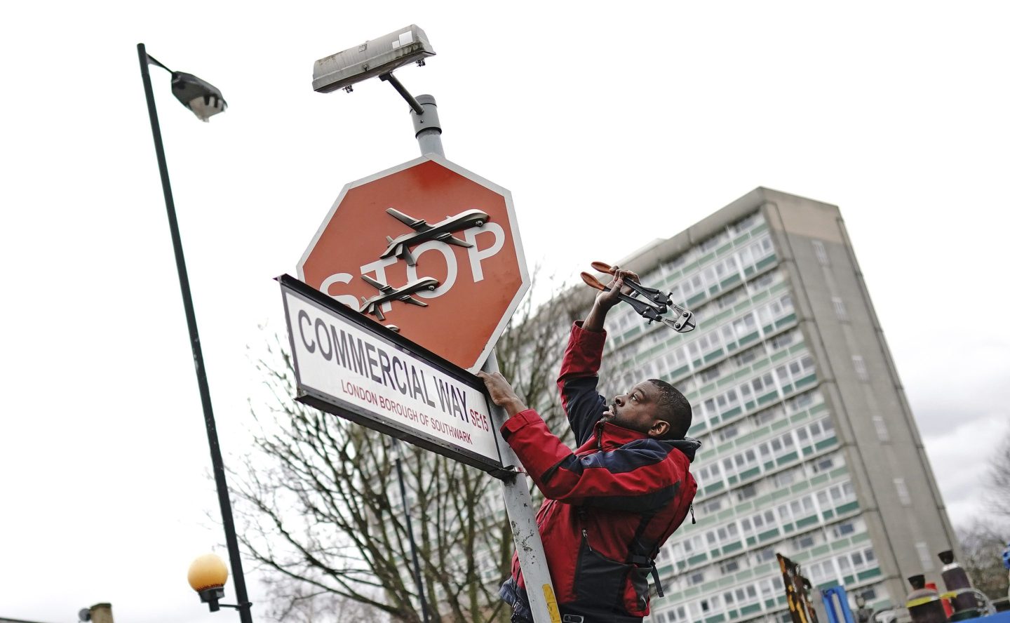 A person removes a piece of art work by Banksy, which shows what looks like three drones on a traffic stop sign, from the intersection of Southampton Way and Commercial Way in Peckham, south east London, Friday Dec. 22, 2023.