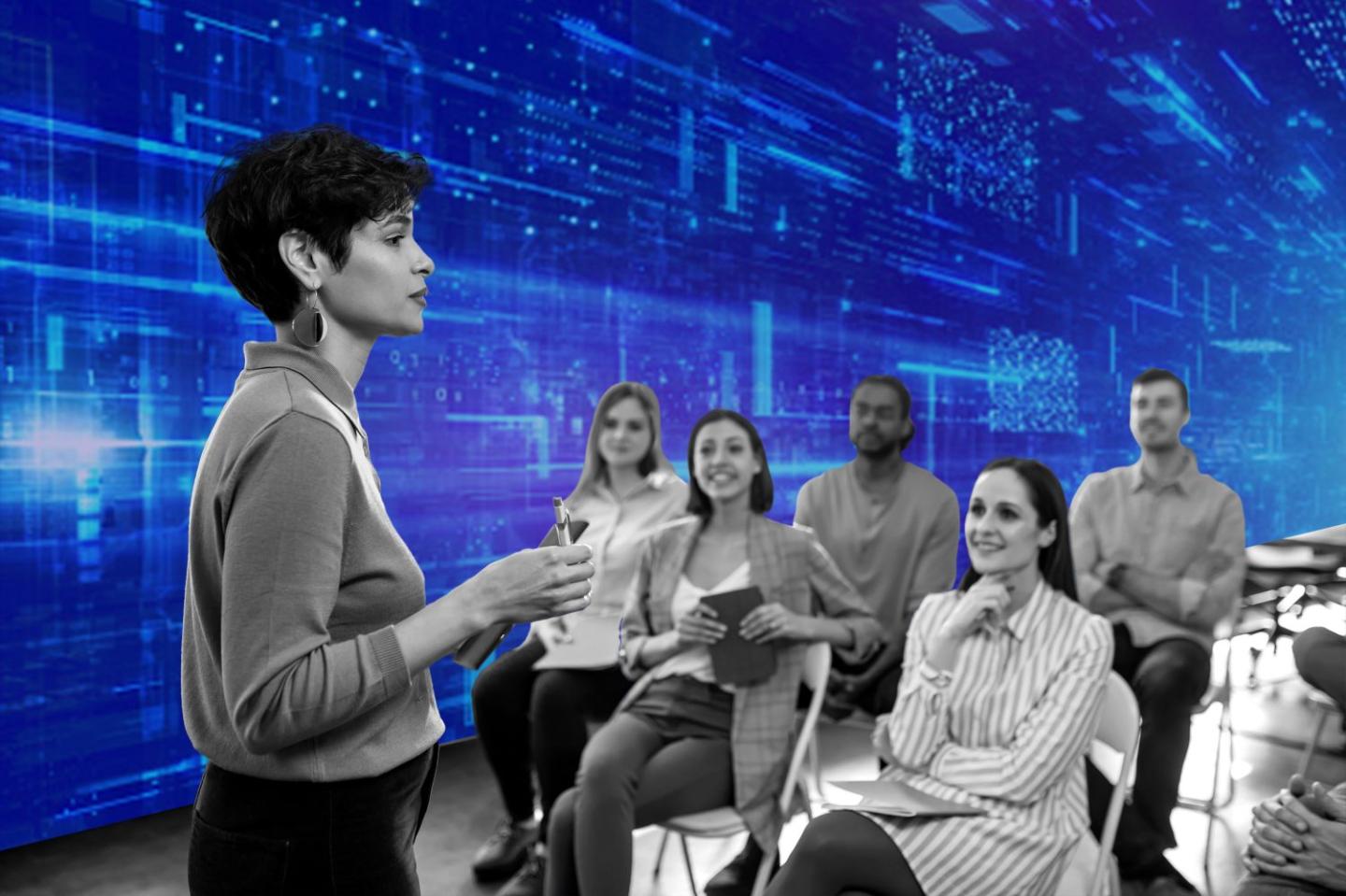 Photo of a business professor addressing her class in front of a screen of AI technology.