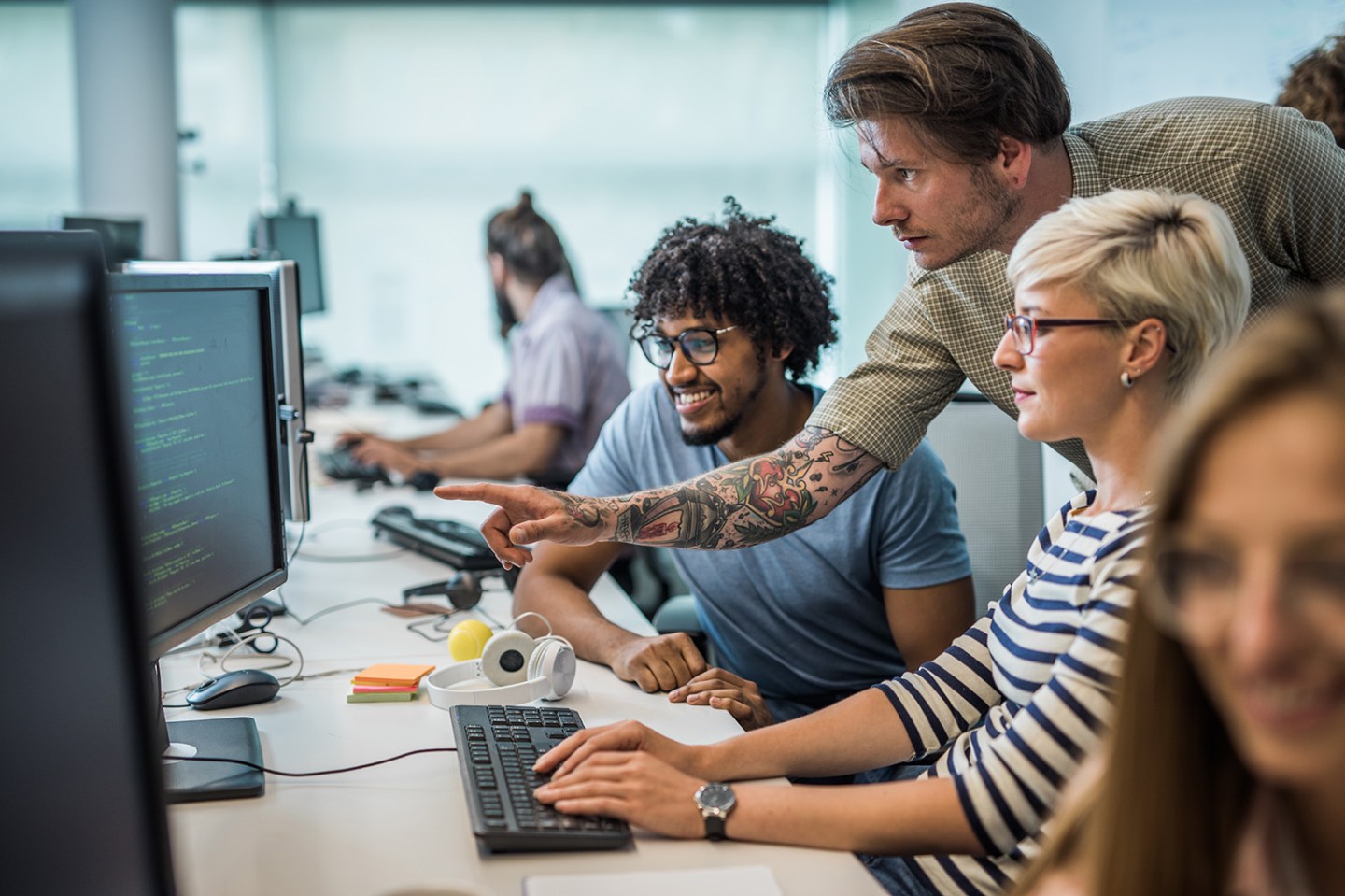 Team of young computer programmers cooperating while working on desktop PC in the office. Focus is on man aiming at computer monitor