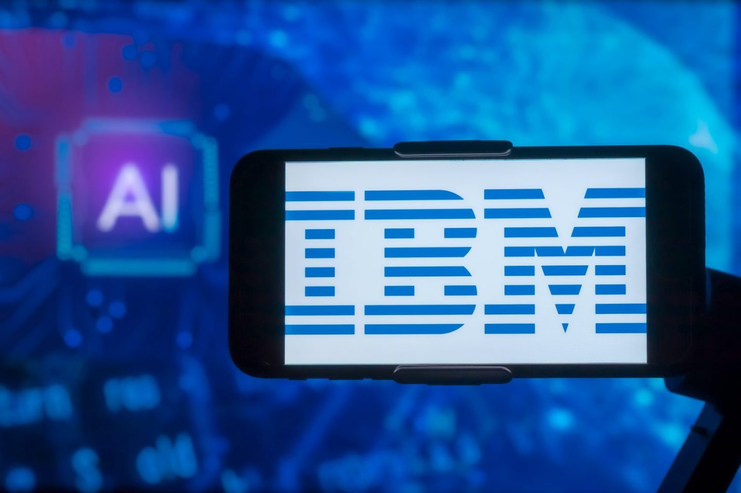 Photo of a smart phone on a stand showing the IBM logo with a bright blue AI screen in the background.