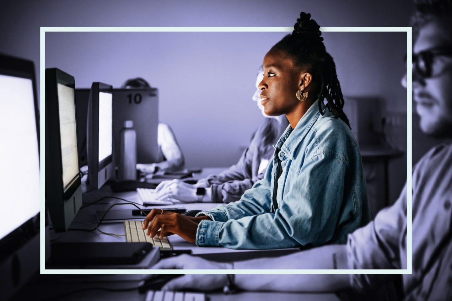 Photo of several young adults sitting at a row of desktop computers studying cybersecurity.