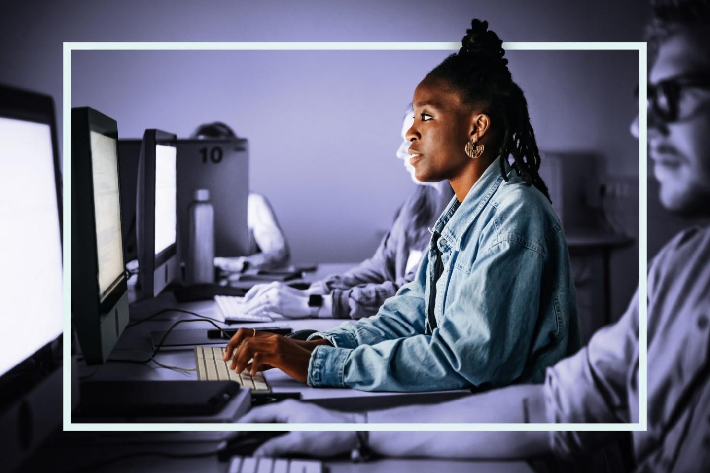 Photo of several young adults sitting at a row of desktop computers studying cybersecurity.