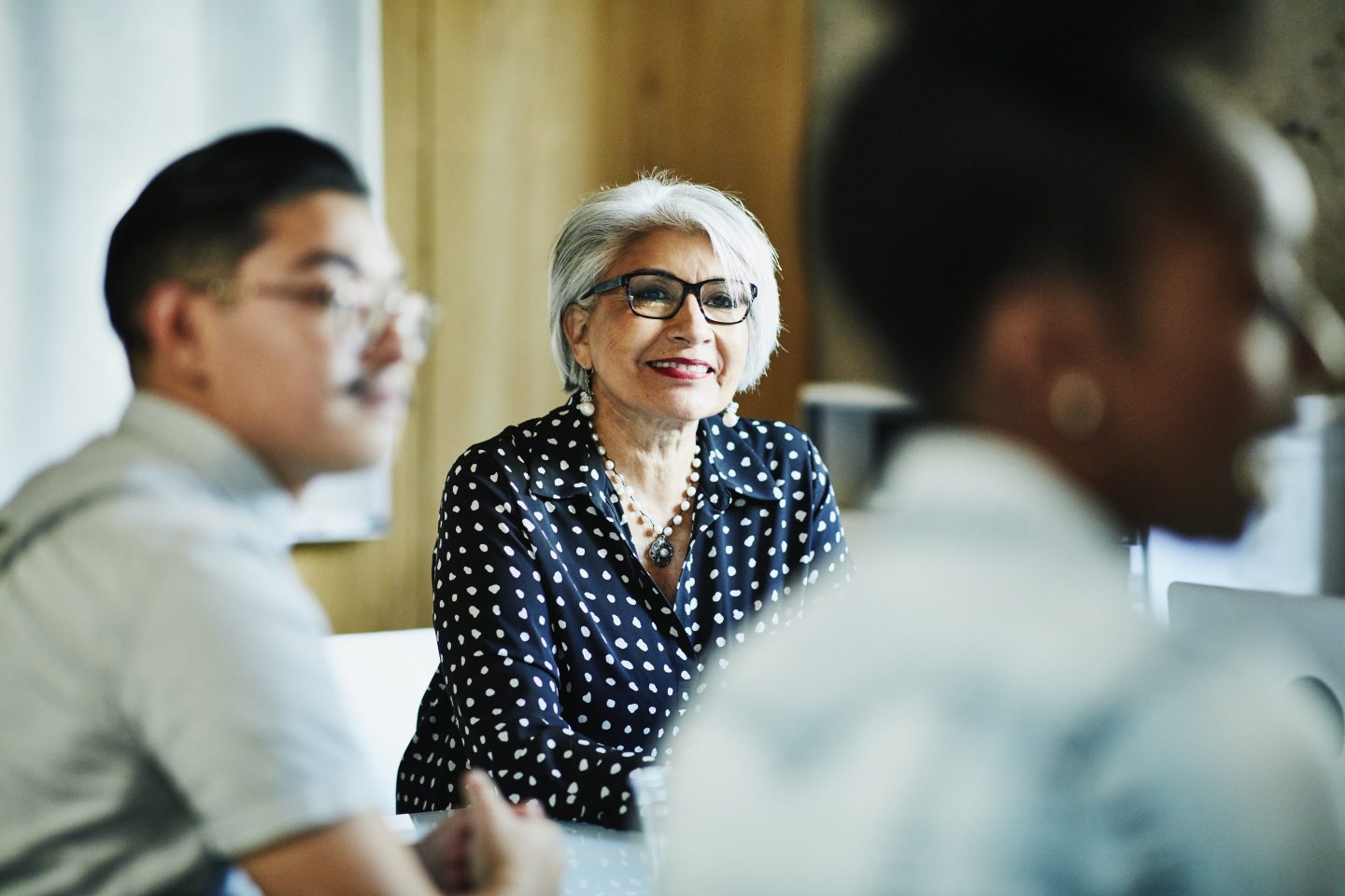 Smiling mature female business owner listening during presentation during meeting in office conference room