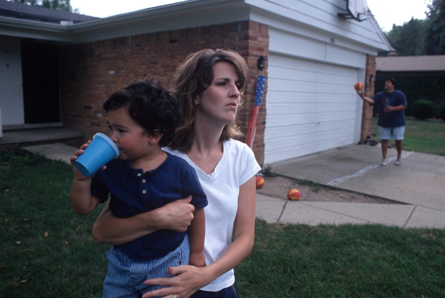 A woman holding a baby outside of her home