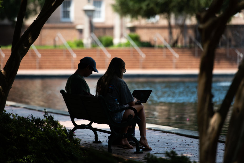 Students sit on a bench in front of the library at the University of South Carolina, as seen in August 2020 in Columbia, South Carolina. (Photo by Sean Rayford/Getty Images)