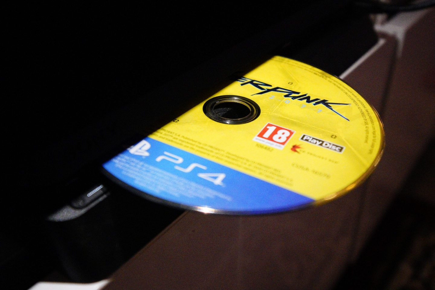 A Cyberpunk 2077 game disc is seen with a Playstation 4 console.