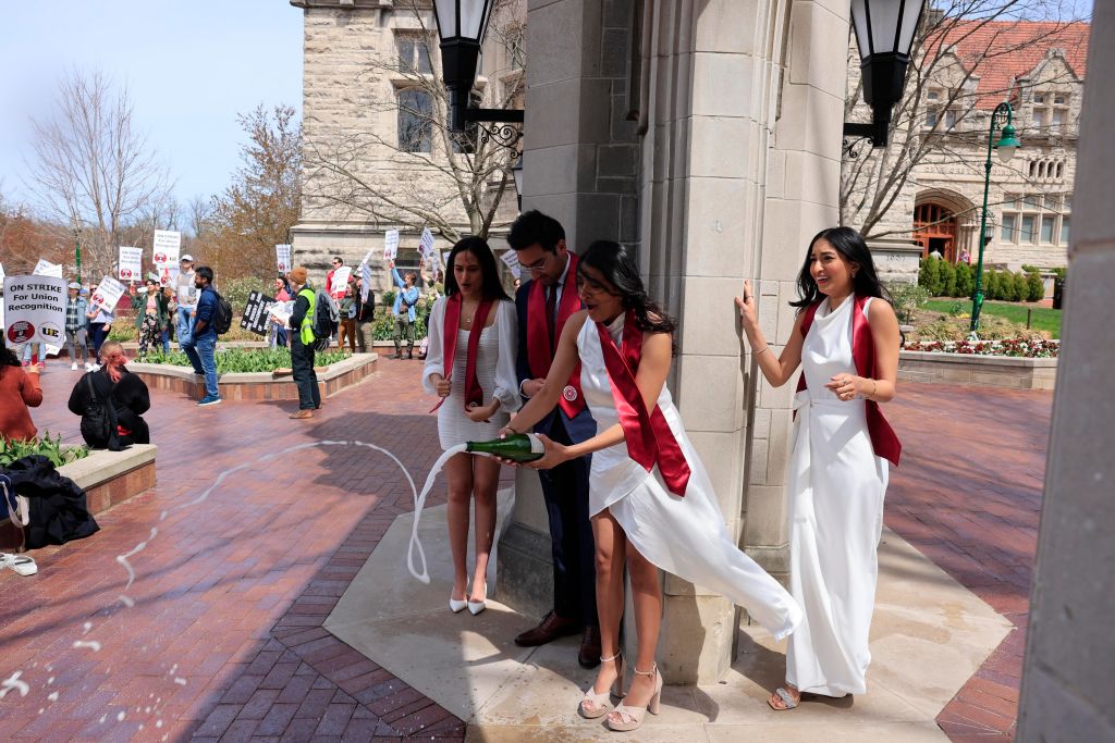 A group of graduating students opened a bottle of Champagne during a photo session at the Sample Gates, as seen in April 2022, in Bloomington, Indiana. (Photo by Jeremy Hogan—SOPA Images/LightRocket/Getty Images)