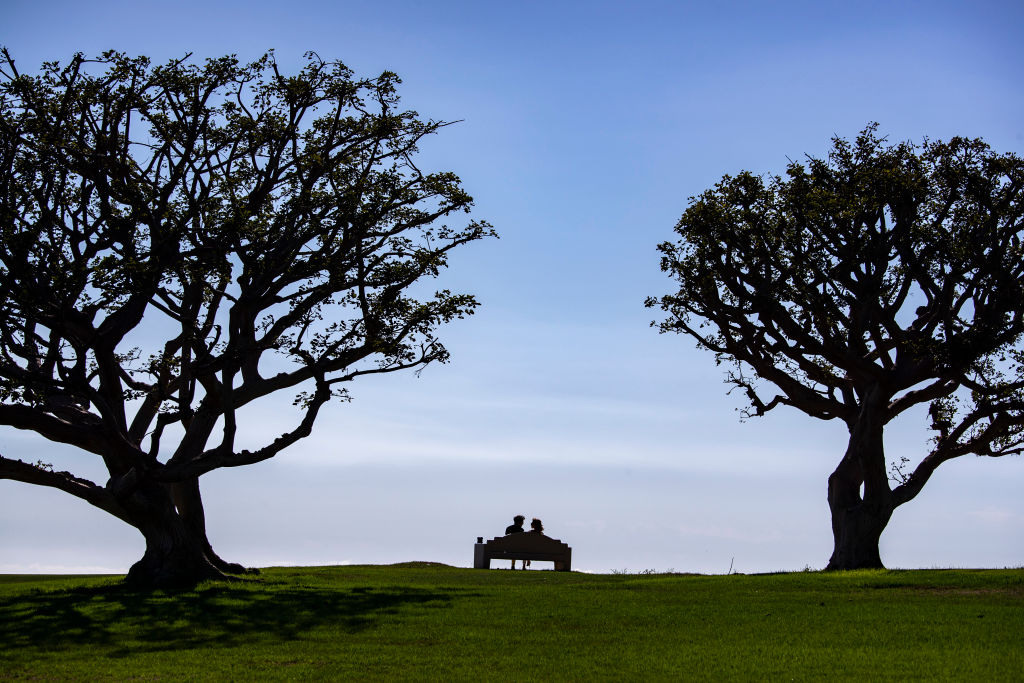 A couple enjoy balmy weather along with an ocean view from a bench on the lawn at Alumni Park at Pepperdine University, as seen in October 2022. (Brian van der Brug—Los Angeles Times/Getty Images)