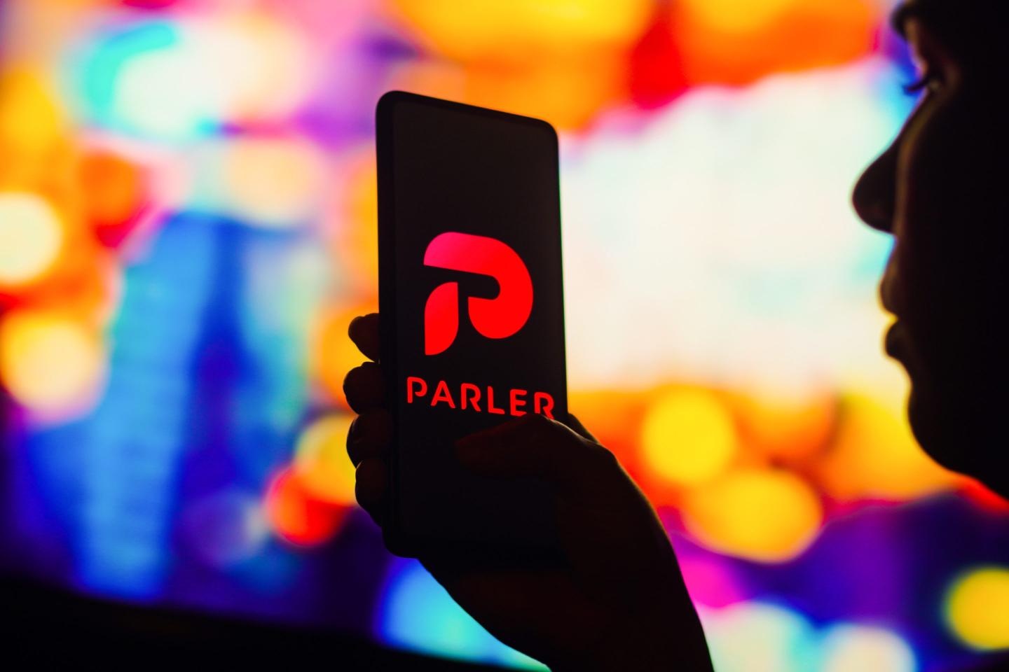 a silhouetted woman holds a smartphone with the Parler logo displayed on the screen