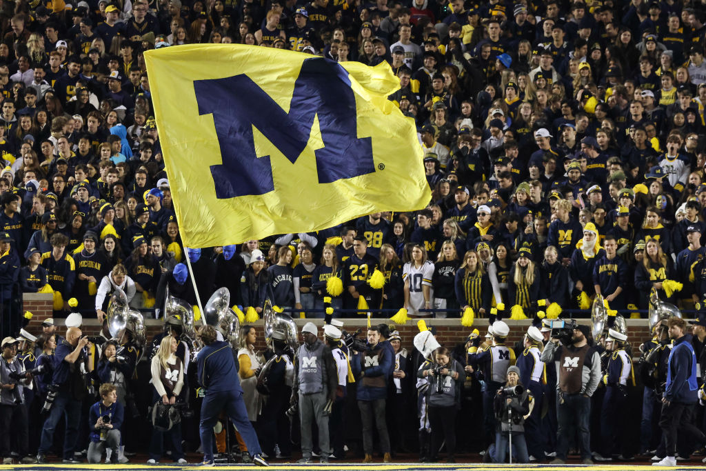 A Michigan cheerleader waves a large flag with the Michigan logo on it during a college football game between the Michigan State Spartans and the Michigan Wolverines, as seen in October 2022 at Michigan Stadium in Ann Arbor, Michigan. (Photo by Scott W. Grau—Icon Sportswire/Getty Images)
