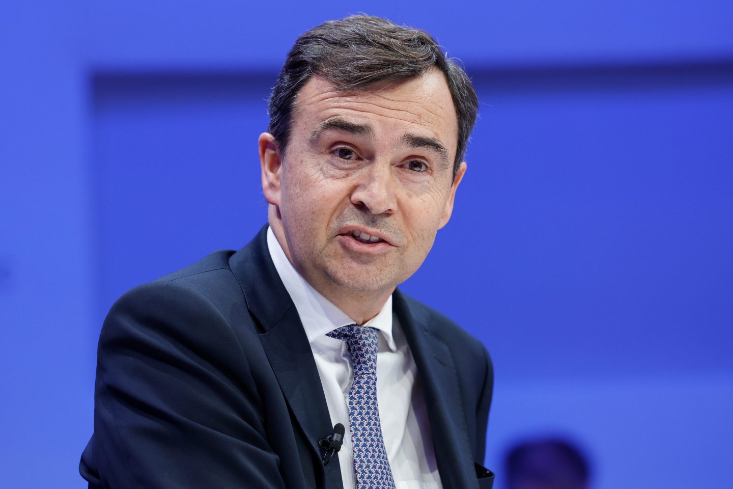 A man wearing a black suit and a blue tie looks towards his right side.