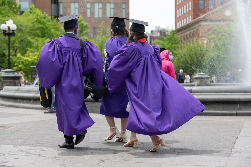 NYU students wearing graduation caps and gowns walk through Washington Square Park, as seen in May 2021. (Alexi Rosenfeld—Getty Images)