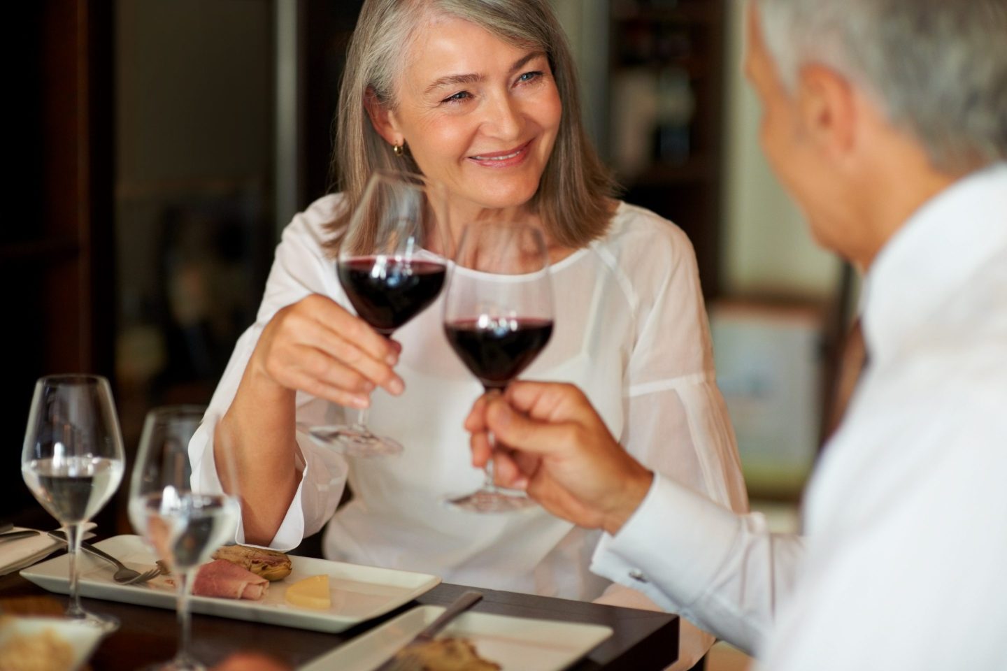 Man and woman with gray hair toasting each other with wine