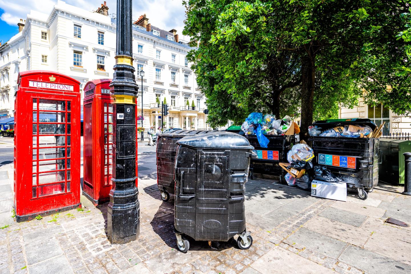 Street scene in London showing a phone booth and trash bins overflowing with garbage