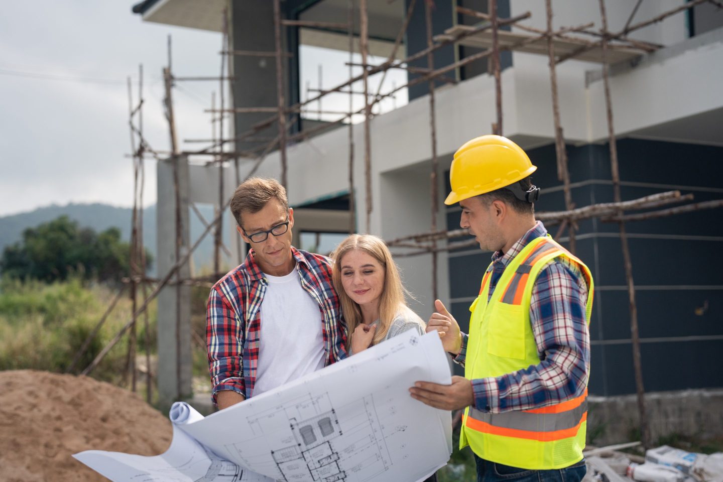 Young couple in front of a home under construction look at floor plans